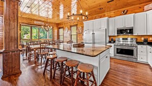 A wooden cabin interior with a central island, bar stools, a kitchen with stainless steel appliances, and a 'WELCOME' sign. - The Majestic Pine Retreat (Gatlinburg)