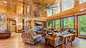 A spacious living area with wooden floors, leather sofas, a stone fireplace, and large windows offering a view of the outdoors. - The Big Oak Lodge (Gatlinburg)