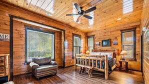 A log cabin bedroom with a bed, a bench, a chair, and a ceiling fan. - The Big Oak Lodge (Gatlinburg)