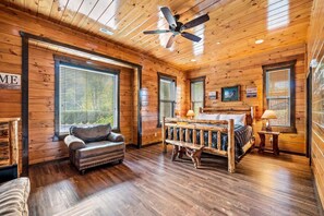 Ein Schlafzimmer in einer Blockhütte mit einem Bett, einer Bank, einem Stuhl und einem Deckenventilator.
