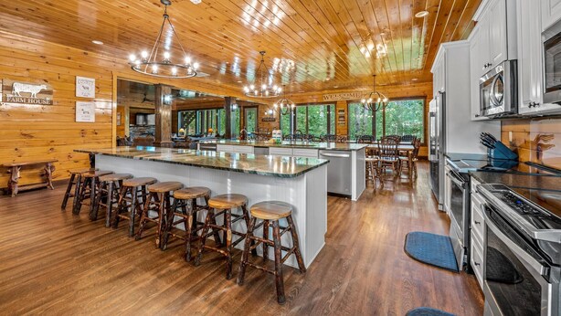 A spacious kitchen with wooden ceilings, a central island with stools, and a view of the outdoors. - The Big Oak Lodge (Gatlinburg)