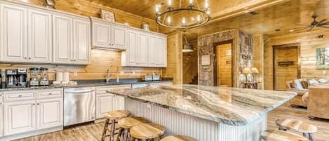 Una cocina con armarios blancos, una isla de mármol con taburetes y un techo de madera.