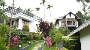 A two-story house with a balcony, surrounded by lush greenery and a stone pathway. - Wild Nest Resort Wayanad (Vythiri)