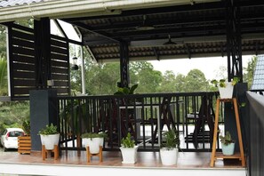 A covered outdoor area with a wooden railing, potted plants, and a car parked nearby. - Wild Nest Resort Wayanad (Vythiri)