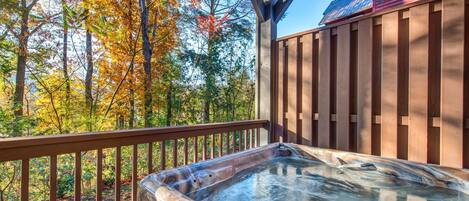 A hot tub on a wooden deck with a view of autumn trees.