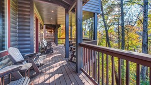 A wooden deck with Adirondack chairs, a covered seating area, and a view of trees. - The Big Poplar Retreat (Gatlinburg)