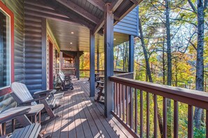 Eine Holzdielen-Terrasse mit Adirondack-Stühlen, einem überdachten Sitzbereich und Blick auf Bäume.