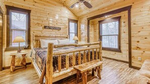 A log cabin bedroom with a bed, two windows, a ceiling fan, and a bench. - The Big Poplar Retreat (Gatlinburg)