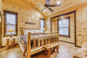 A log cabin bedroom with a bed, two windows, a ceiling fan, and a bench. - The Big Poplar Retreat (Gatlinburg)