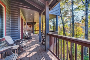 Une terrasse en bois avec des fauteuils Adirondack, un espace salon couvert et une vue sur les arbres.