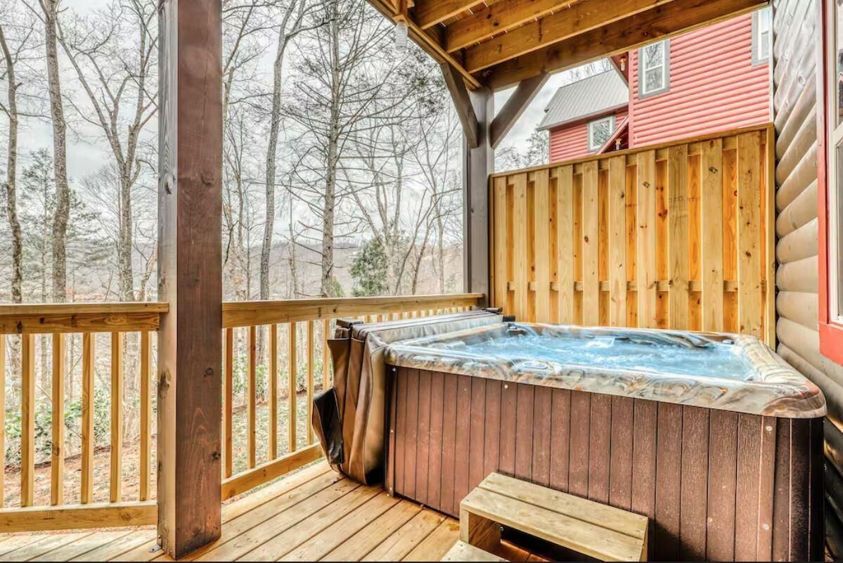 Un jacuzzi en una terraza de madera con vista a árboles y un edificio rojo al fondo.