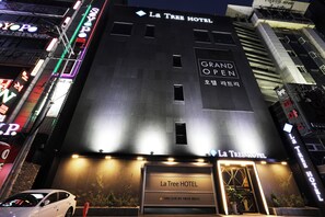 La Tree Hotel with a prominent entrance, a sign for Grand Open, and surrounding neon signs.