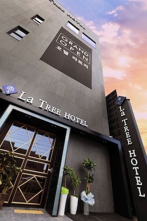The exterior of La Tree Hotel with a modern design, large windows, and potted plants.