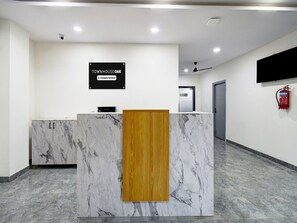 Ein Empfangsschalter mit Marmorplatte und Holzpaneel, ein Schild mit der Aufschrift 'Townhouse Oak Company-Serviced', ein Deckenventilator und ein Feuerlöscher an der Wand.