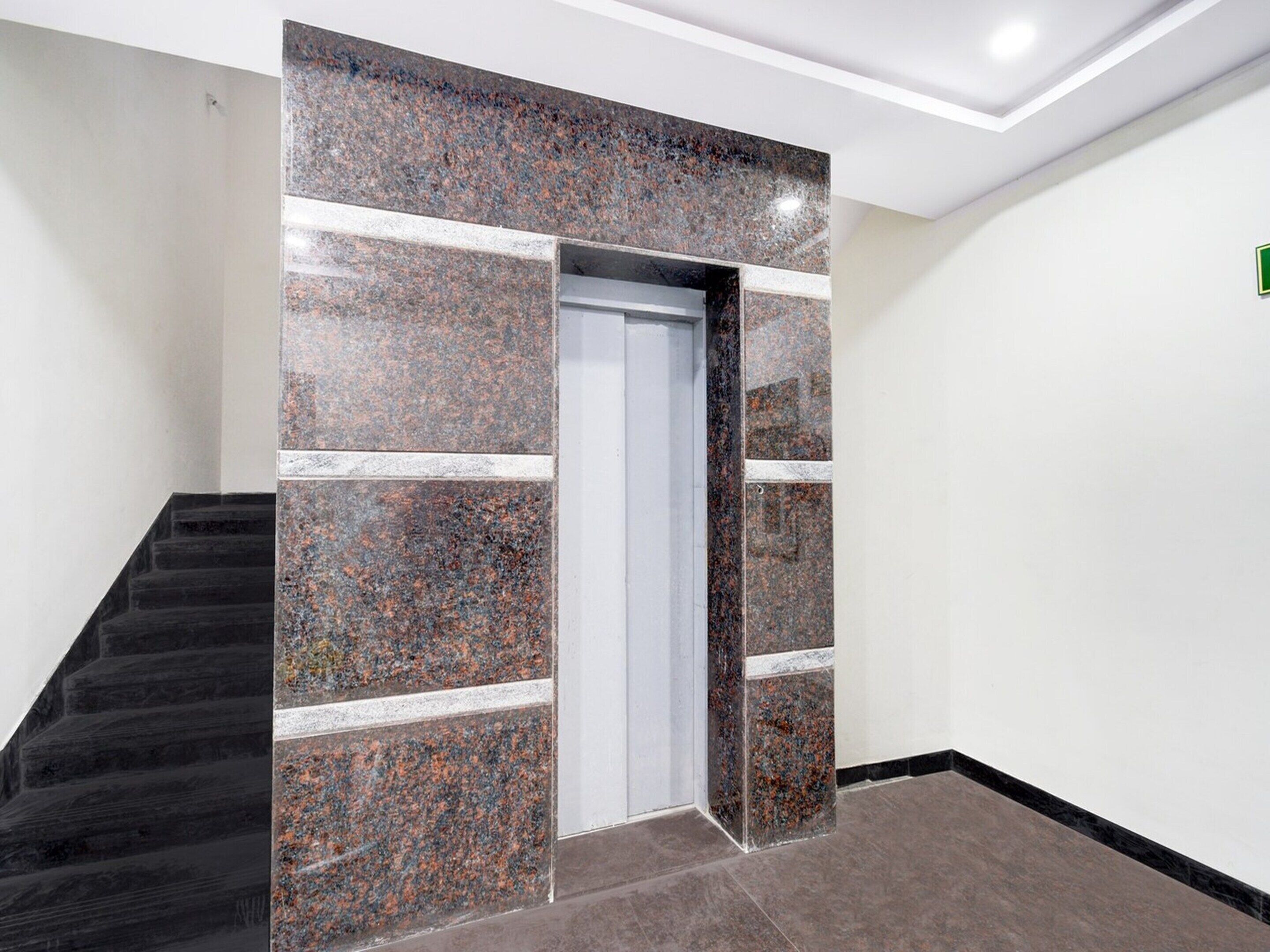 Ein modernes Interieur mit einer Treppe, einer Tür mit Marmorwand und einer schlichten weißen Wand mit einem grünen Schild.