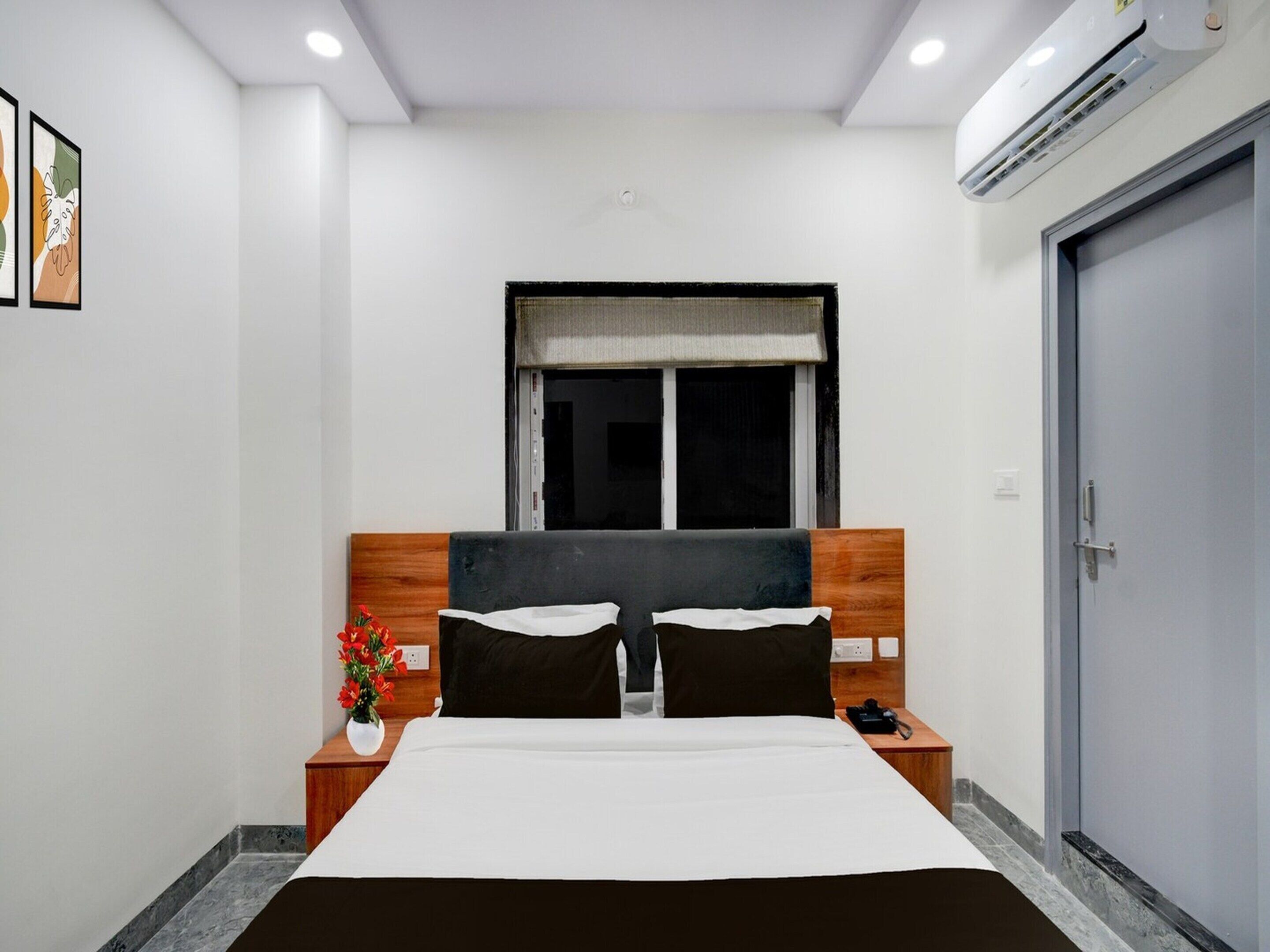 A hotel room with a bed, bedside tables, a window, and an air conditioning unit.