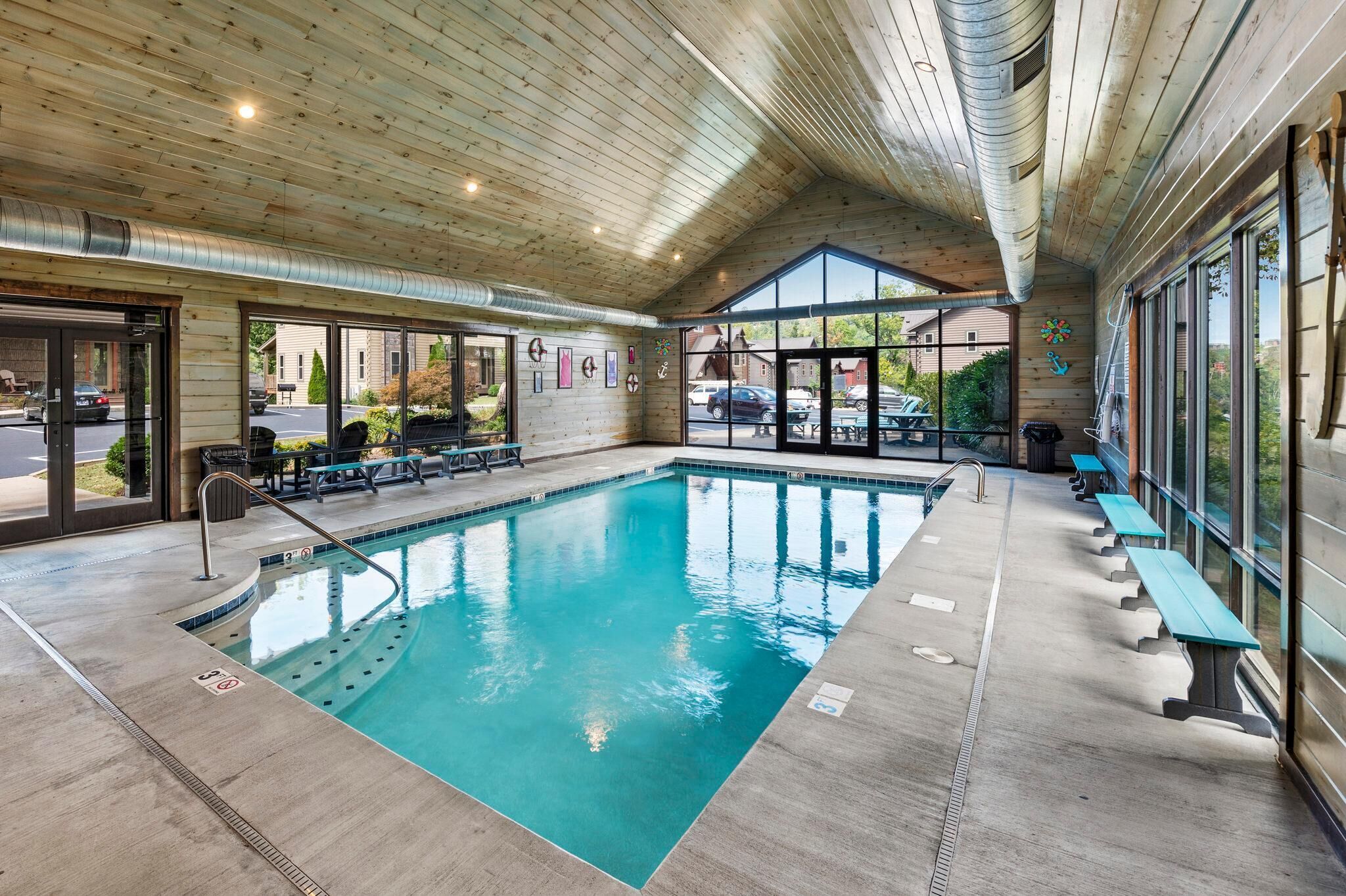 Una piscina interior con techo de madera, bancos y vistas al exterior.
