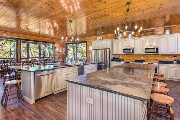 A spacious kitchen with wooden cabinets, stainless steel appliances, and a large island with stools. - The Grand Orchard Lodge (Gatlinburg)