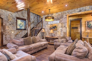 A rustic interior with a wooden staircase, plush sofas, a 'Welcome' sign, and a wooden door. - The Grand Orchard Lodge (Gatlinburg)
