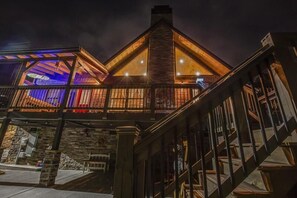 A building with a prominent wooden staircase, a balcony with railings, and a stone facade. - The Aspen Cabin (Gatlinburg)
