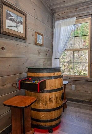 A wooden interior with a barrel, a small table, and a window with curtains. - The Aspen Cabin (Gatlinburg)