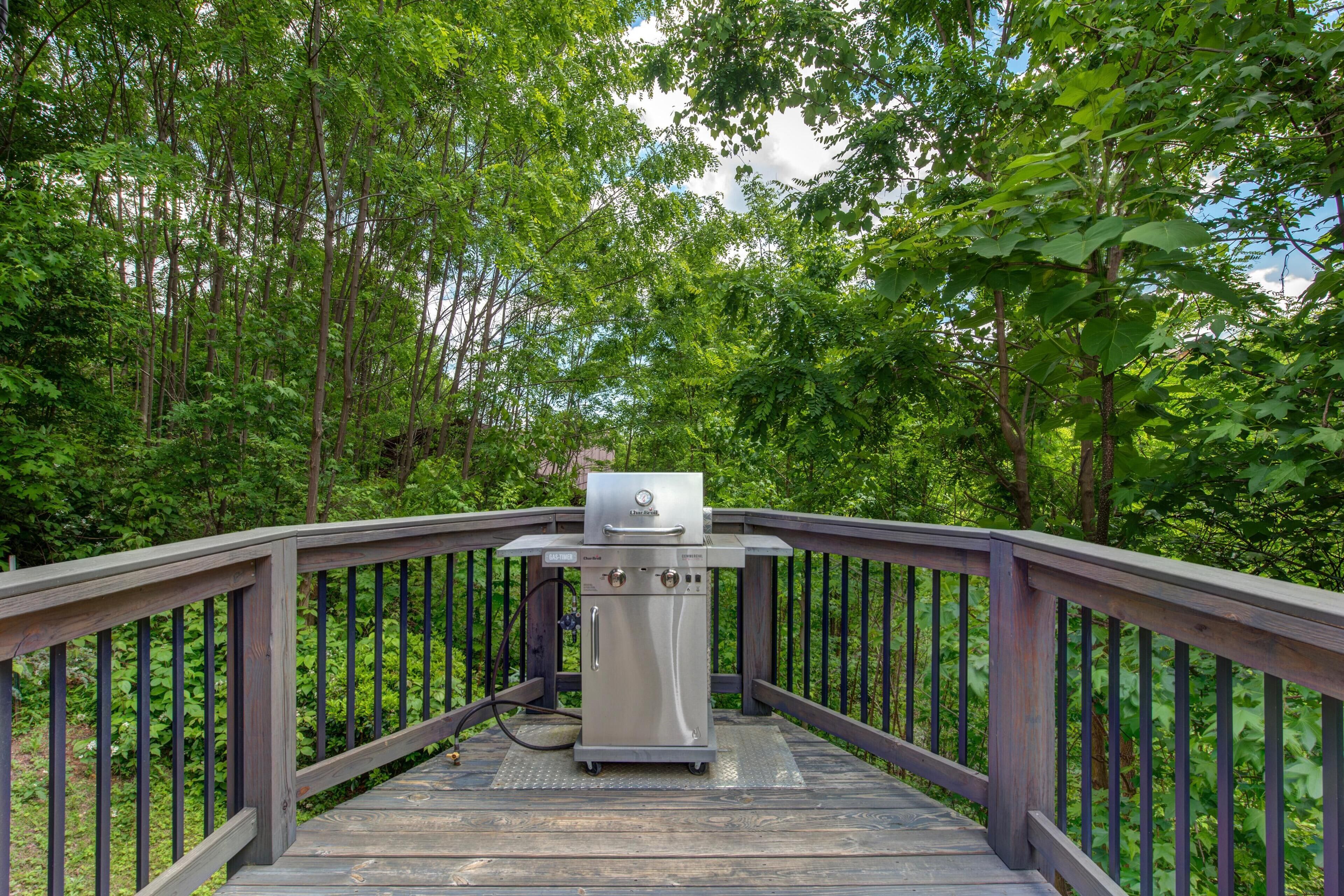 A grill on a wooden deck surrounded by trees.
