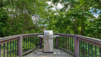 A grill on a wooden deck surrounded by trees.