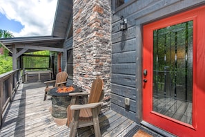 A deck with a stone pillar, a red door, and a fire pit with chairs. - The Aspen Cabin (Gatlinburg)