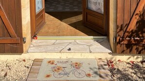 A wooden door with a welcome mat featuring a bicycle and sunflowers. - 3-star air-con gîte - 5 mins by foot to Monpazier at the heart of the bastides. (Capdrot)