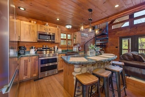 Una cocina con armarios de madera, microondas, estufa y una isla de piedra con taburetes.