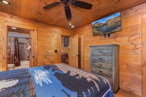 Quarto de cabana de madeira com cama, ventilador de teto, televisão e armário.
