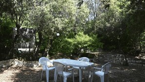 Eine Terrasse mit Tisch und Stühlen, umgeben von Bäumen und einer Steinmauer.