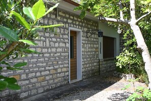 A stone building with a wooden door and a window, surrounded by greenery.