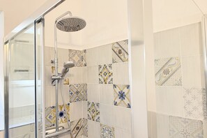 Een douche met een glazen deur, een handdouche en een wand met patroon betegelde tegels.