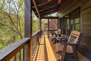 A wooden deck with a railing, benches, and a view of trees and a red building. - Black Bear Cabin (Gatlinburg)