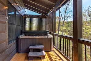 A wooden deck with a hot tub, wooden benches, and a railing overlooking a forested area. - Black Bear Cabin (Gatlinburg)