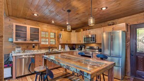 A wooden interior with a central island, bar stools, a stainless steel refrigerator, and a microwave. - Black Bear Cabin (Gatlinburg)