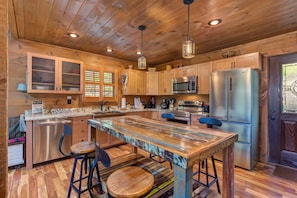 A wooden interior with a central island, bar stools, a stainless steel refrigerator, and a microwave. - Black Bear Cabin (Gatlinburg)