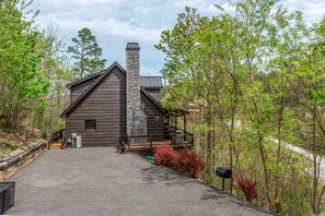 A log cabin with a stone chimney, a porch, and a view of the surrounding forest. - Black Bear Cabin (Gatlinburg)