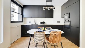 Una cocina moderna con armarios oscuros, una mesa redonda de comedor, sillas de mimbre y una lámpara colgante.