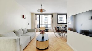 Una sala de estar moderna con un sofá, una mesa redonda de centro, un comedor con sillas y un ventanal grande.