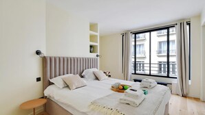 Habitación de hotel con cama, una mesita, una ventana con cortinas y vistas a edificios.