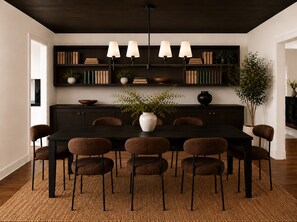 A dining area with a dark wooden table, six brown chairs, a woven rug, and a bookshelf with books and plants. - NEW! Lux Sedona Stay • Hot Tub • Views • Game Room (Sedona)