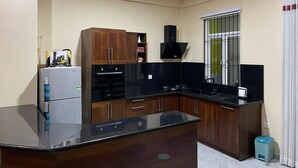 A compact kitchen with a refrigerator, oven, stove, wooden cabinets, and a window with bars. - Cozy 1-bedroom bungalow in quaint Polgasowita with AC (Polgasowita)