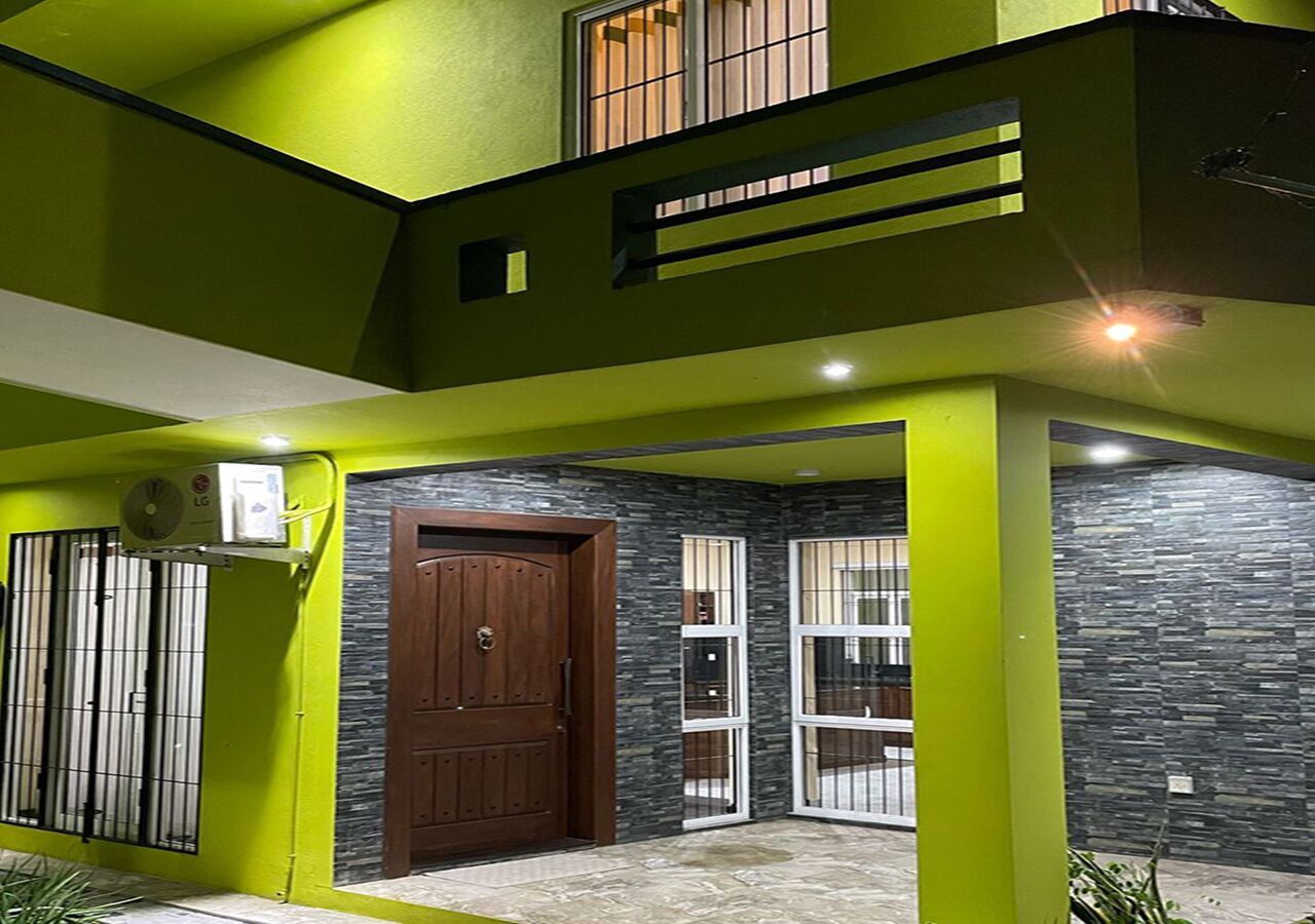 A modern house with a green exterior, a wooden door, and a window with bars.. Cozy 1-bedroom bungalow in quaint Polgasowita with AC