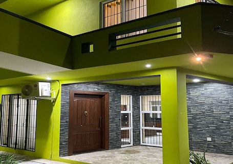 A modern house with a green exterior, a wooden door, and a window with bars.. Cozy 1-bedroom bungalow in quaint Polgasowita with AC