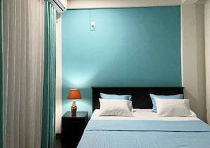 Ein Hotelzimmer mit Bett, Nachttisch, Lampe und Wandklimaanlage.