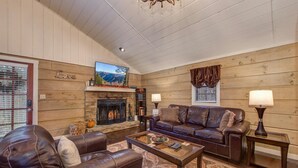 A cozy living room with a fireplace, leather sofas, a coffee table, and a television mounted above the fireplace. - Seclusion Retreat (Gatlinburg)