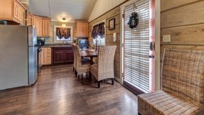 A kitchen with wooden cabinets, a refrigerator, a microwave, a dining table with chairs, and a wicker bench. - Seclusion Retreat (Gatlinburg)