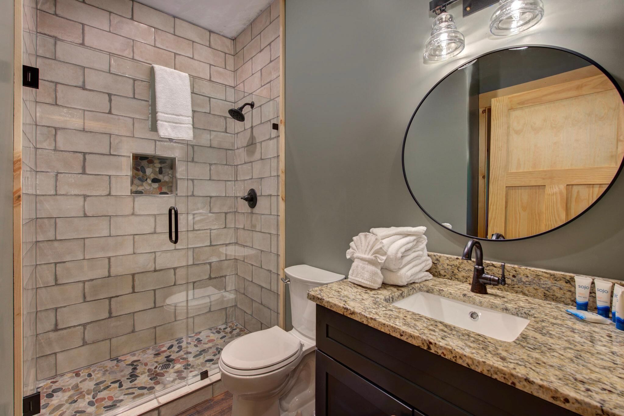 A bathroom with a shower, toilet, sink, and mirror.